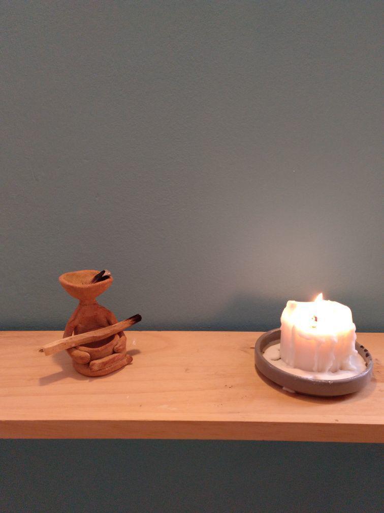 A very zen-looking bowlhead with an incense stick on its lap. It sits with legs crossed and next to it there is a lit up candle.