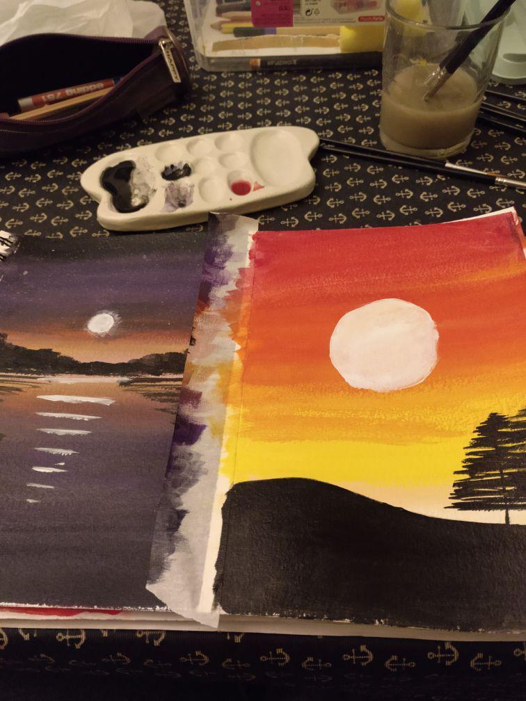 Two paintings in the foreground: a sunrise to the left and a sunset to the right. Behind them there is a paint mixing palette with some colours and brushes.