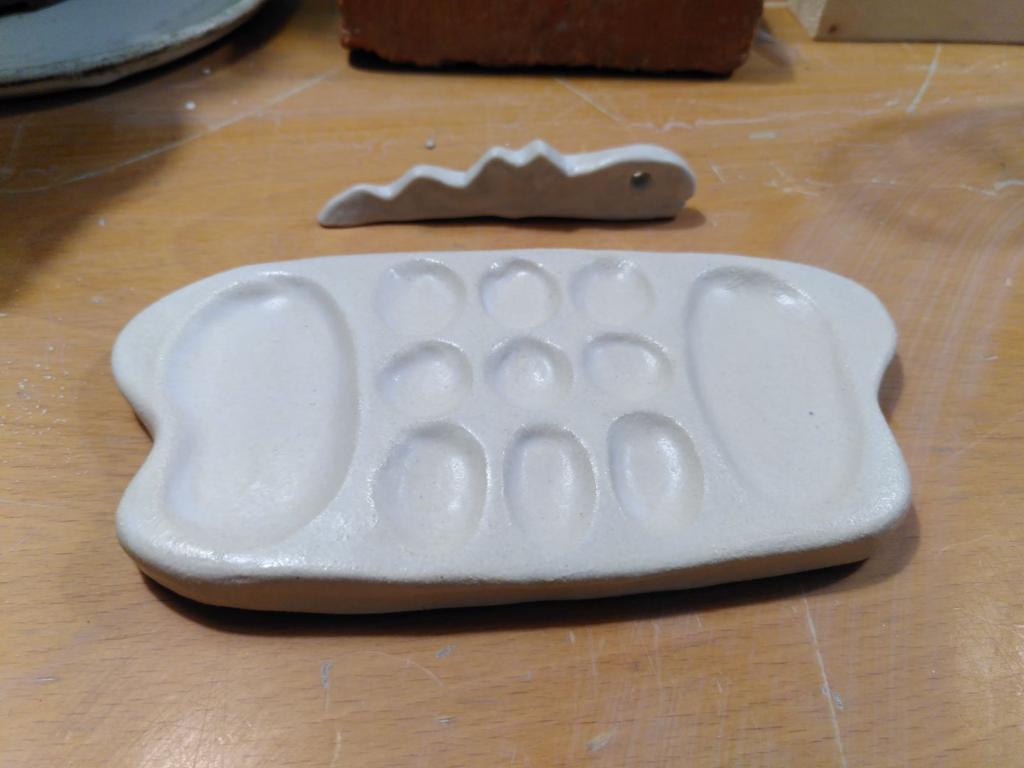 The paint mixing palette shaped as a butterfly, with two big pools to the sides (butterfly's wings) and 9 smaller pools in the middle.
Right behind it, there is a snake-shaped brush holder, which has a hole for an eye and an open mouth.