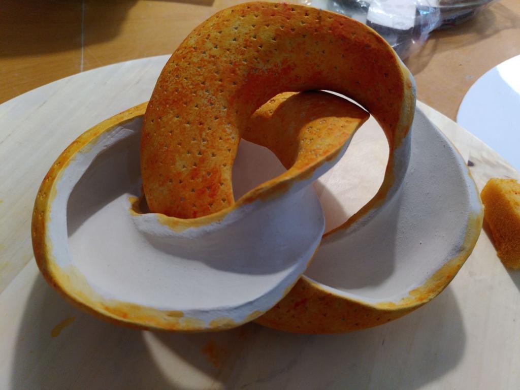 The doughnut, open. It is two interlaced separate pieces, but the interior is still not painted, so it is light orange out + white inside.