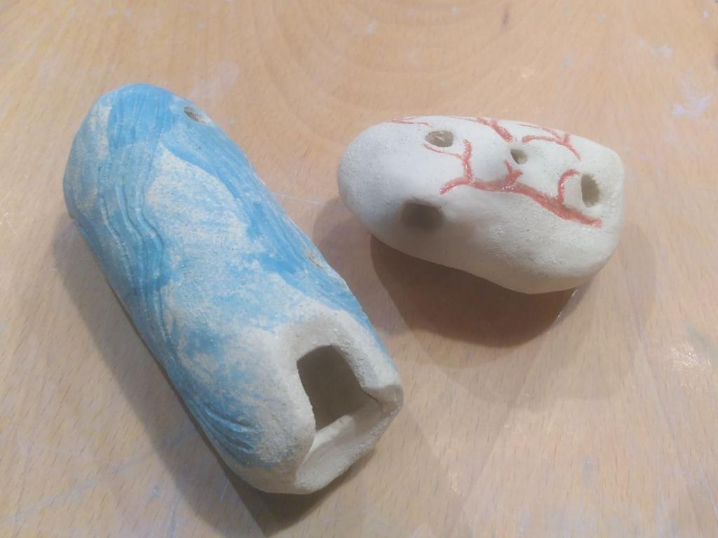 A blue ocarina with tubular in shape, four holes to the side and one at the bottom. The other is heart shaped has 3 holes and red lines.