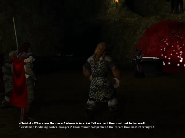 Virstania, amb un pentinat curiós que semblen banyes i un vestit molt llarg, just darrere una mena d'altar on a sobre està la peça Arcana i més enrere una mena de cova vermella i uns puntets de llum que es mouen.